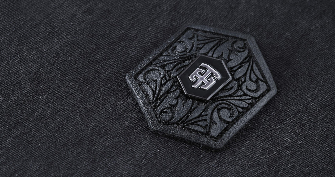 Close-up of THEODORE signature badge featuring engraved ornamental detailing on a premium luxury men's jacket, showcasing refined craftsmanship and designer branding.