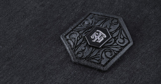 Close-up of THEODORE signature badge featuring engraved ornamental detailing on a premium luxury men's jacket, showcasing refined craftsmanship and designer branding.