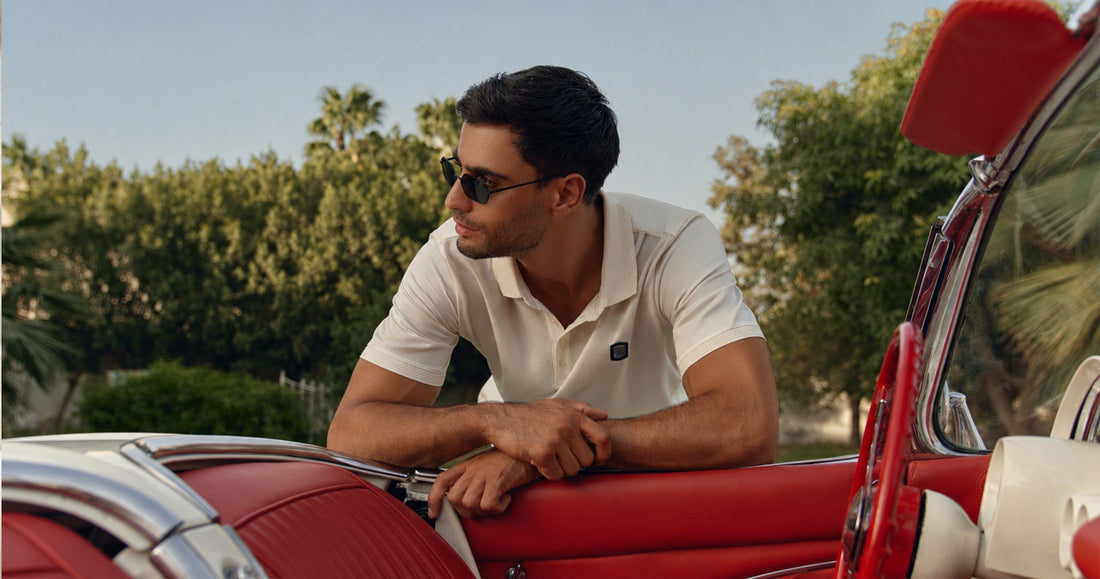 Man wearing cream THEODORE polo shirt leaning on a red vintage convertible, capturing relaxed luxury and refined summer style