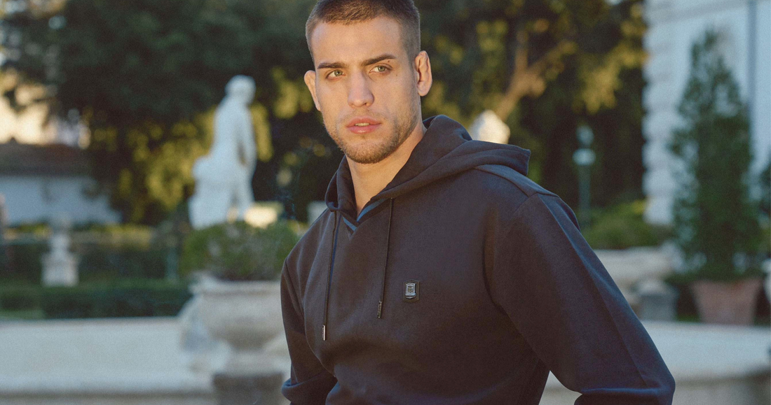 Man wearing a Navy THEODORE hoodie and tailored trousers in an outdoor estate setting, showcasing refined casual menswear and modern individuality.