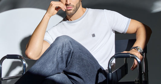 Man wearing a white THEODORE premium T-shirt with signature chest badge, seated in a director’s chair under dramatic natural light, showcasing the brand’s refined minimalism
